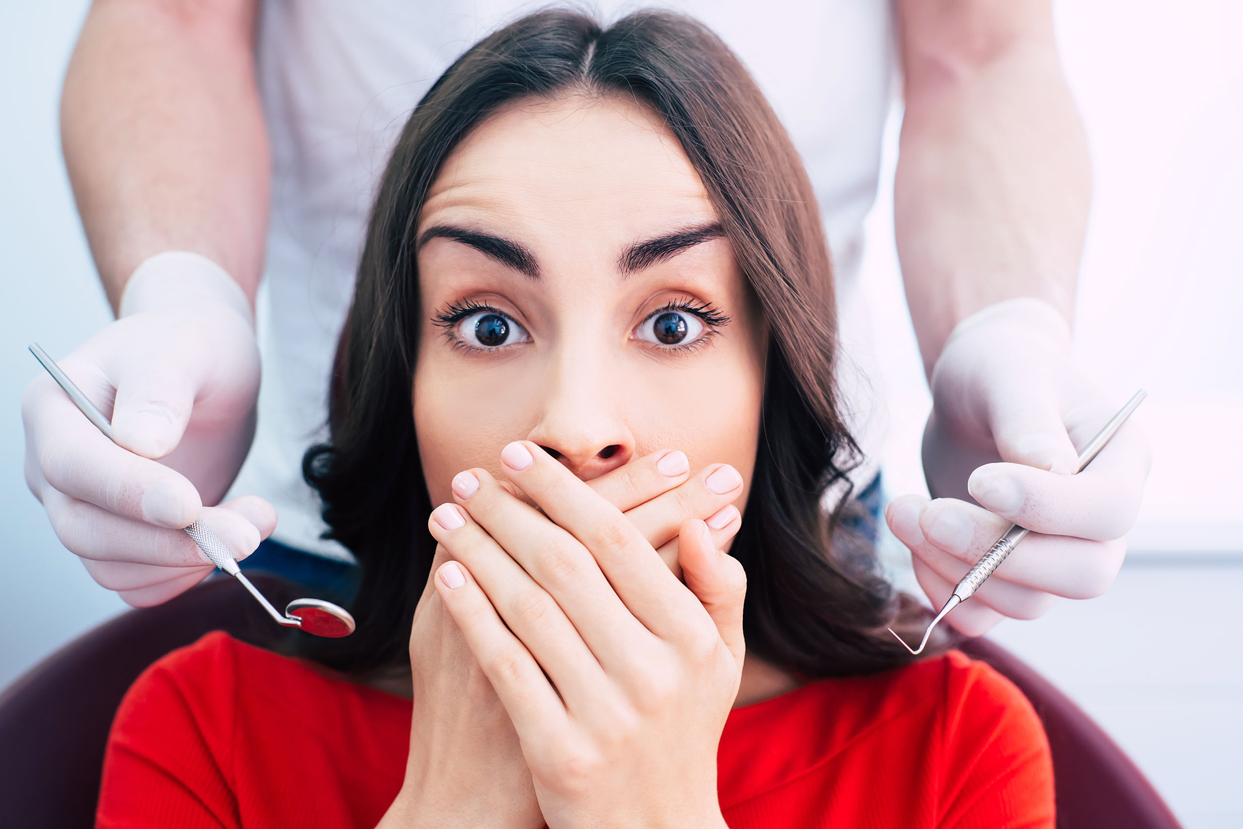 Anxious woman covering her mouth as a dentist holds mirror and probe before an exam. Our Yuba City dentist provides gentle, comfortable care.