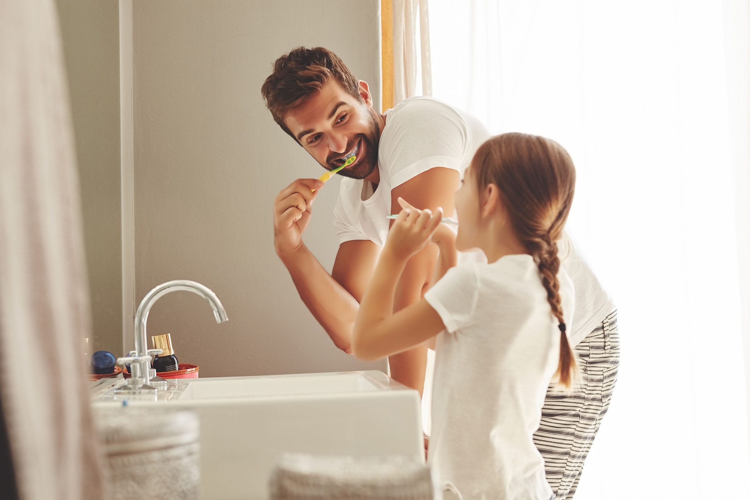 Adult and child brushing teeth together at a bathroom sink, demonstrating daily oral hygiene routine