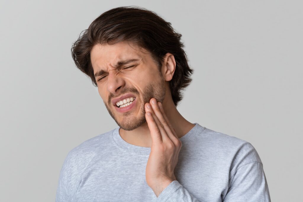 Man in a great long sleeve shirt clenching his jaw indicating jaw pain.