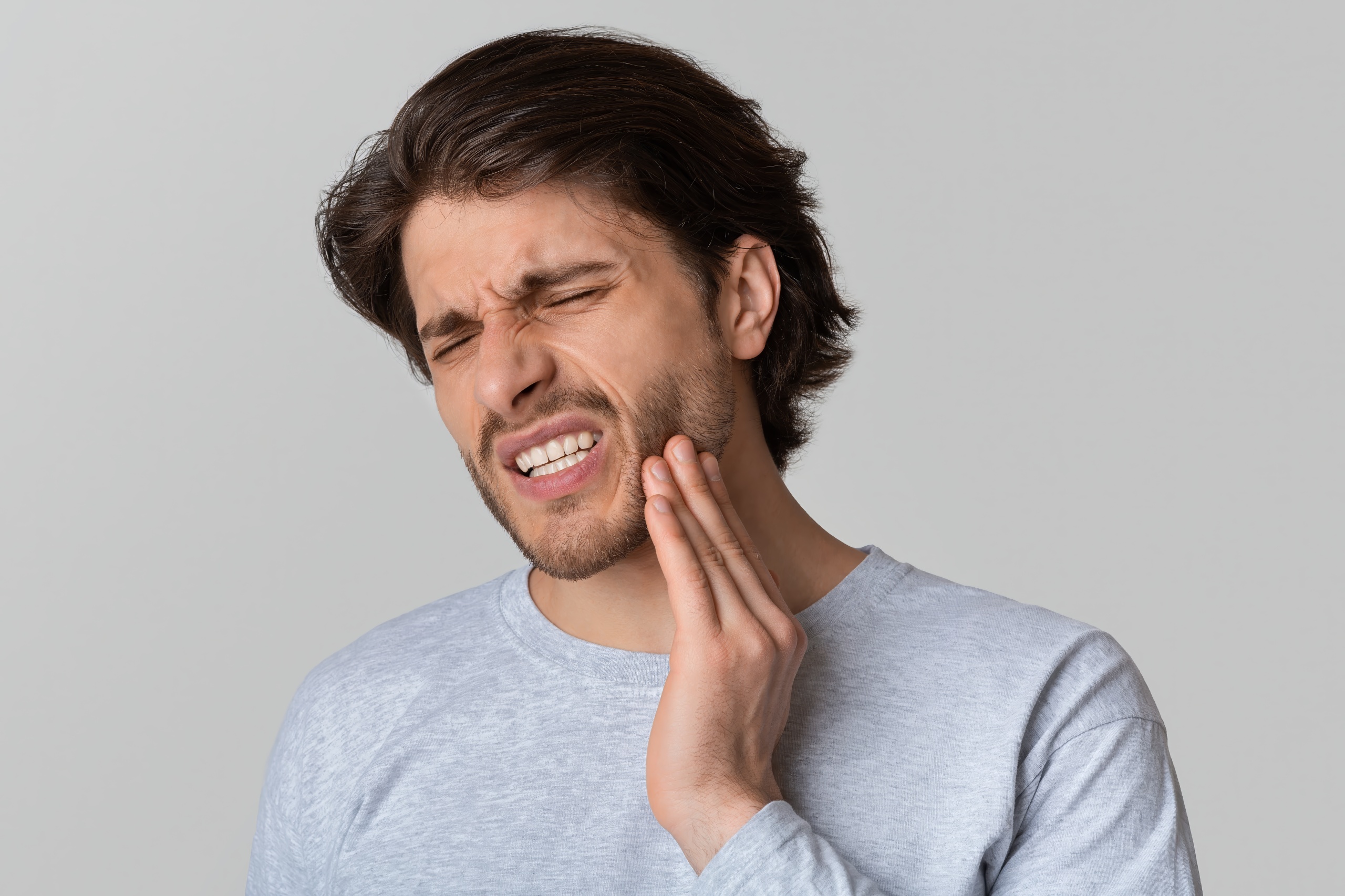 Dental problems concept. Man suffering from toothache Man in a great long sleeve shirt clenching his jaw indicating jaw pain.